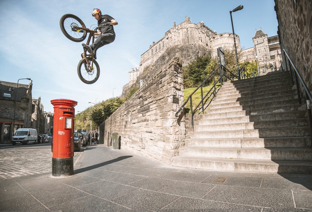 Danny Macaskill jumping a large gap from a high wall to a postbox